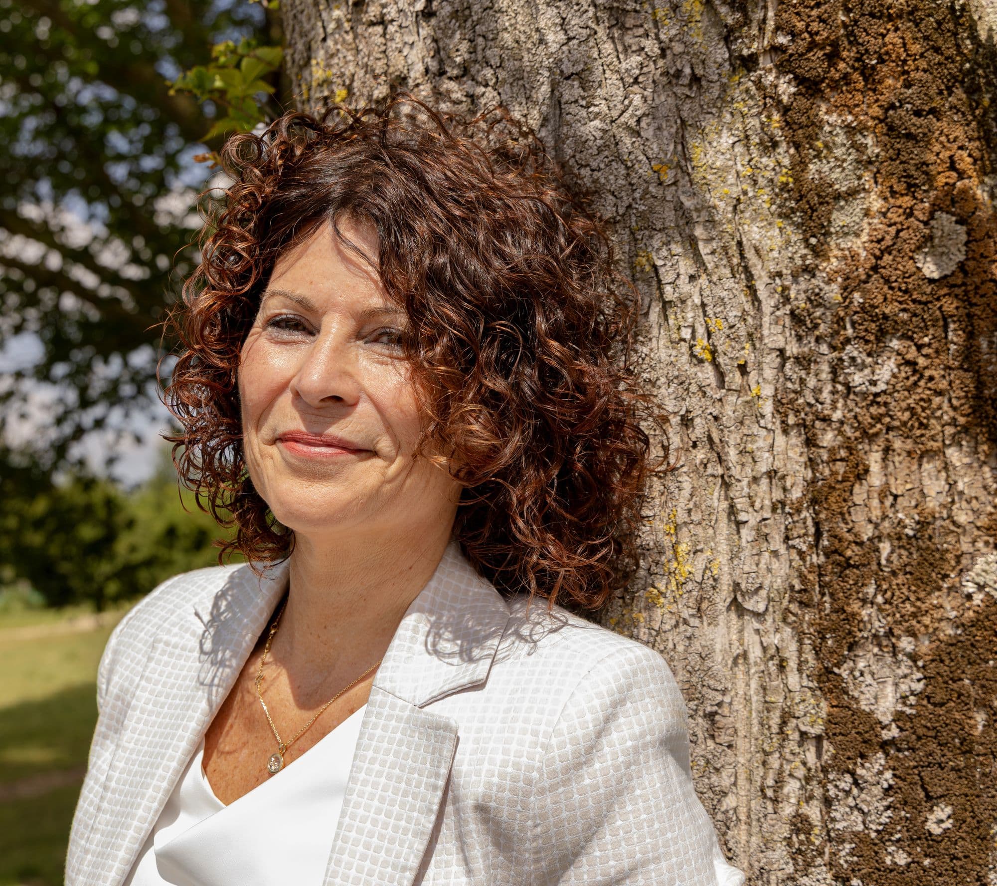 Jeanine, vertrouwenspersoon bij Confidence Talk, tegen een boom in het zonlicht